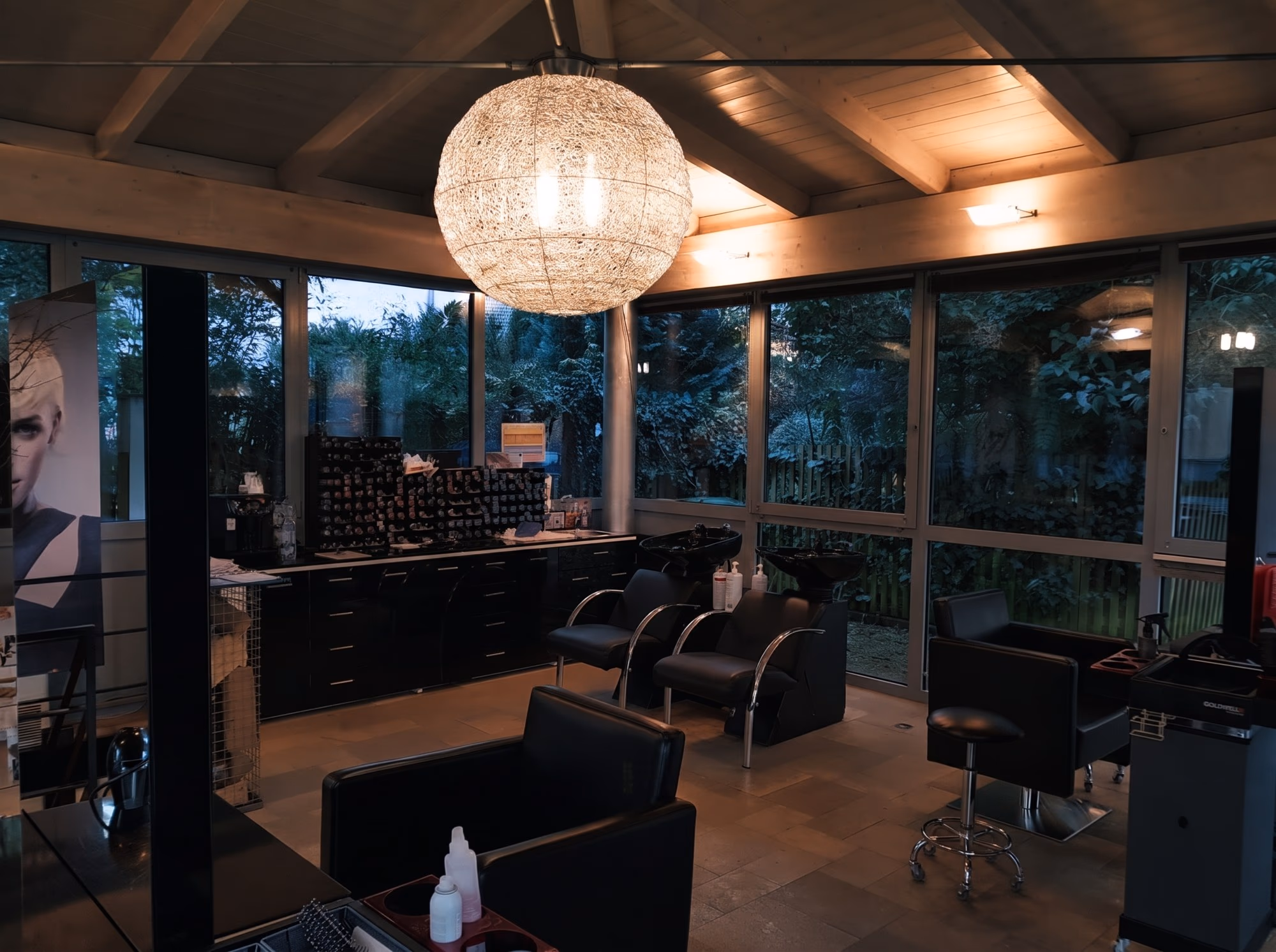 Der Salon Haar Exakt am Abend von innen, Kugelleuchte und schwarze Sessel